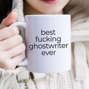 May include: White ceramic coffee mug with black text that reads "best fucking ghostwriter ever".