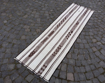 May include: A white and brown striped runner rug with geometric patterns. The rug is made of wool and has a hand-woven texture.