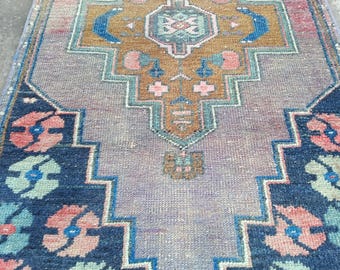 May include: A rectangular, vintage-style rug with an intricate geometric pattern. The rug features a central design in shades of brown, pink, and blue, surrounded by a navy blue border with floral motifs. The rug's overall color palette is muted.