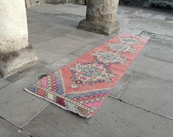 May include: A rectangular, vintage-style runner rug with a coral-colored background and intricate geometric and floral patterns in shades of blue, pink, and green. The rug is displayed on a stone surface.