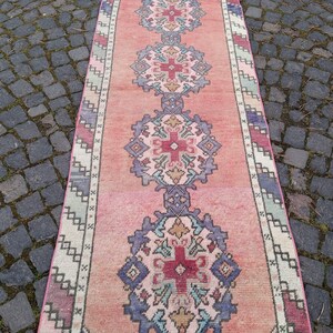 以下が含まれることがあります： 伝統的な花柄のヴィンテージピンクとクリームのランナーラグ。ラグは色あせていて、ウール製です。