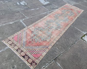 May include: A vintage runner rug with a faded pink, blue, and cream color scheme. The rug has a traditional Persian design with intricate details and a floral pattern.