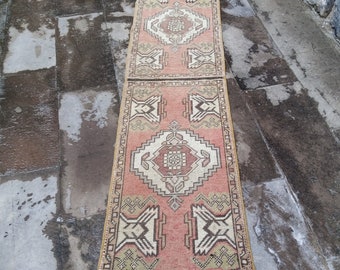 May include: A long, narrow rug with a traditional Turkish design. The rug is in shades of pink, beige, and brown. It has a fringe on both ends.