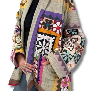 Peut inclure: Veste patchwork avec une variété de motifs floraux et géométriques colorés. La veste présente une base beige clair avec des accents de violet, rose, jaune et marron. La veste a une coupe décontractée et un col châle.