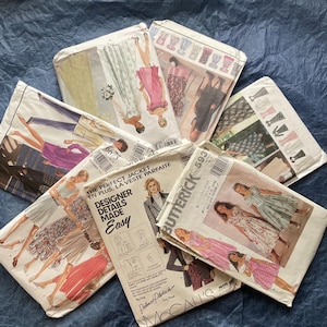 May include: A collection of vintage sewing patterns for dresses and jackets. The patterns are in various colors and designs, including floral, plaid, and geometric patterns. The patterns are labeled with the brand names Butterick and McCall's.