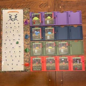 May include: A board game setup with various components. Includes a game board with a skull and crossbones, cards, and plastic holders in purple, blue, and green. There are also small game pieces in various colors, and cards with illustrations.