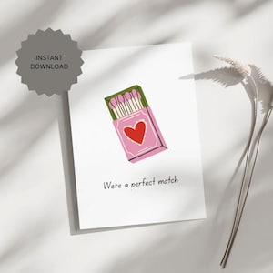 May include: A white greeting card featuring a pink matchbox illustration with a red heart and a row of matches with pink tips. The text "Were a perfect match" is printed in black below the illustration. A grey "INSTANT DOWNLOAD" badge is visible.