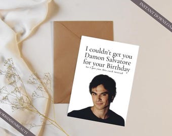 Può includere: Un biglietto d'auguri bianco con la fotografia di un uomo dai capelli scuri e il testo stampato in nero: I couldn't get you Damon Salvatore for your Birthday, So I got you this card instead. Il biglietto è accanto a una busta marrone.