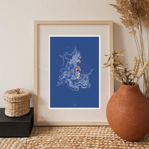Pode incluir: Impressão artística emoldurada com um desenho a traço branco de um navio sobre um fundo azul. As velas do navio são adornadas com formas abstratas coloridas. A obra de arte é exibida em uma moldura de madeira clara, com uma cesta tecida e um vaso de terracota em primeiro plano.