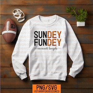 Peut inclure: Sweat-shirt blanc avec le texte "SUNDEY FUNDEY cincinnati bengals" en noir et orange à rayures de tigre. Un ballon de football et du papier décoratif sur une surface en bois.