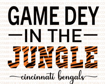 May include: A graphic design featuring the text "GAME DEY IN THE JUNGLE" in bold black and orange tiger stripe font. Below, the words "cincinnati bengals" are written in a cursive font. The design includes "PNG/SVG" and a social media handle.