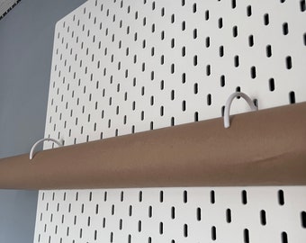 May include: A white pegboard with a brown paper roll hanging from two white hooks. The roll is held in place by the hooks.