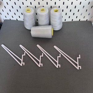 May include: Four white spools of thread with yellow tops, sitting on a gray surface. Three white plastic shelf brackets are also on the surface.
