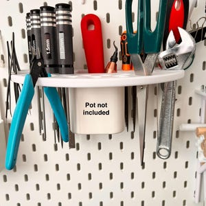 May include: A white pegboard organizer with various tools. Includes blue handled pliers, screwdrivers, scissors, a wrench, and other small tools. A white pot with the text "Pot not included" is also present.