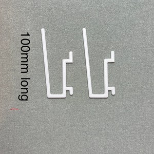 May include: Two white plastic shelf brackets, each measuring 100mm long. The brackets are designed to support shelves.