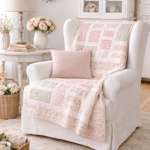 Puede incluir: Un sillón blanco con una colcha de retazos rosa y verde. Una almohada rosa a juego descansa sobre la silla. La habitación está decorada con flores, una lámpara y una mesa auxiliar, creando un ambiente acogedor y acogedor.