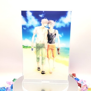 Puede incluir: Un soporte acrílico transparente con una colorida ilustración de dos personas caminando por una playa. La obra de arte representa un día soleado con cielo azul y océano. El soporte está sobre una plataforma giratoria blanca, rodeada de cristales de colores.