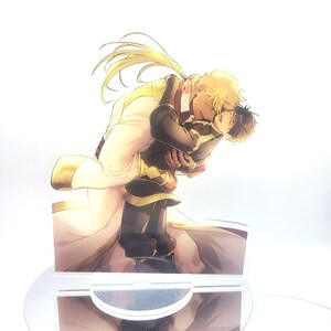 May include: A clear acrylic stand with a printed image of two men embracing. The man on the left is wearing a white and gold robe, while the man on the right is wearing a black and gold outfit. The image is set against a white background.