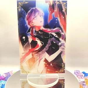 May include: A clear acrylic stand with a vibrant anime-style illustration of a person in a black dress and pink hair. The artwork has a dramatic, fantasy theme, set on a reflective base.