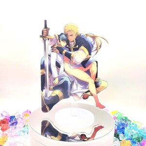 May include: A clear acrylic stand with a light inside, featuring a two-dimensional image of two men embracing. The man on the left is wearing a white shirt and blue pants, while the man on the right is wearing a blue and gold shirt and pants. The man on the right is holding a sword.