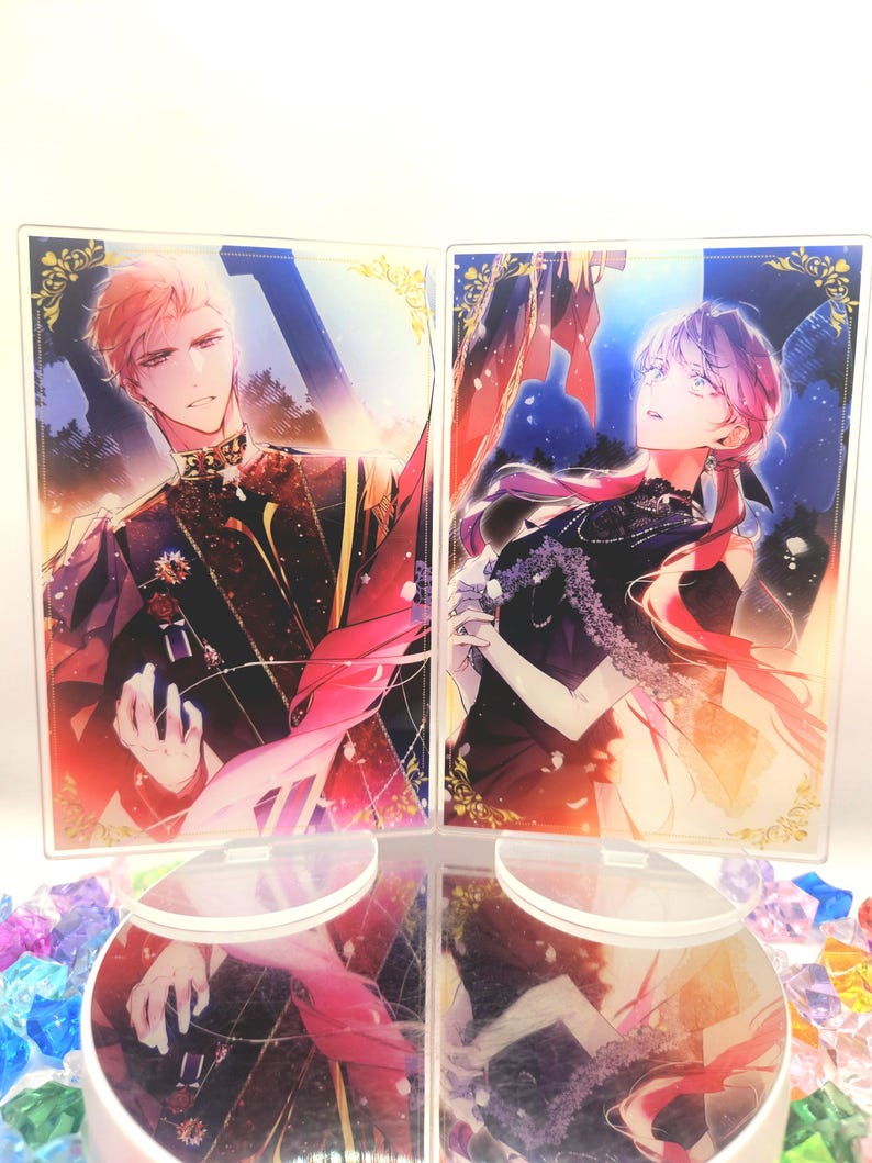 May include: Two acrylic display stands with anime-style illustrations of a man and a woman. The man is in a dark uniform with gold details, the woman in a black dress. Both have colourful hair and are set against a vibrant background.