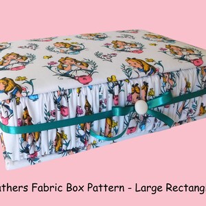 May include: A white fabric box with a teal ribbon and a white button closure. The box is decorated with a repeating pattern of Alice in Wonderland characters and flowers. The box is labelled "Gathers Fabric Box Pattern - Large Rectangle".