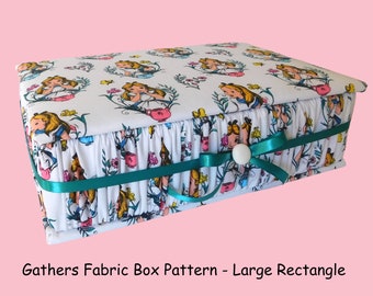 May include: A white fabric box with a teal ribbon and a white button closure. The box is decorated with a repeating pattern of Alice in Wonderland characters and flowers. The box is labeled "Gathers Fabric Box Pattern - Large Rectangle".