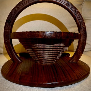 May include: A dark brown wooden serving tray with a decorative handle and a tiered, collapsible bowl. The tray has a circular base and a carved design around the handle.