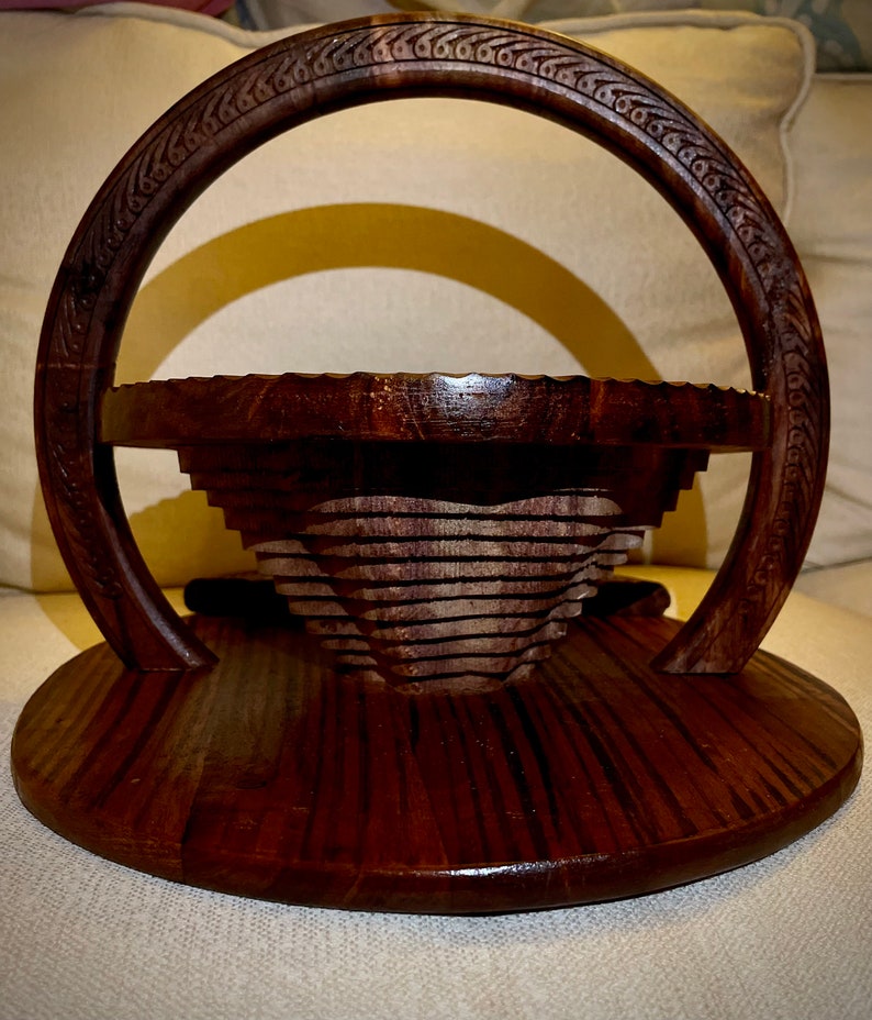 May include: A dark brown wooden serving tray with a decorative handle and a tiered, collapsible bowl. The tray has a circular base and a carved design around the handle.