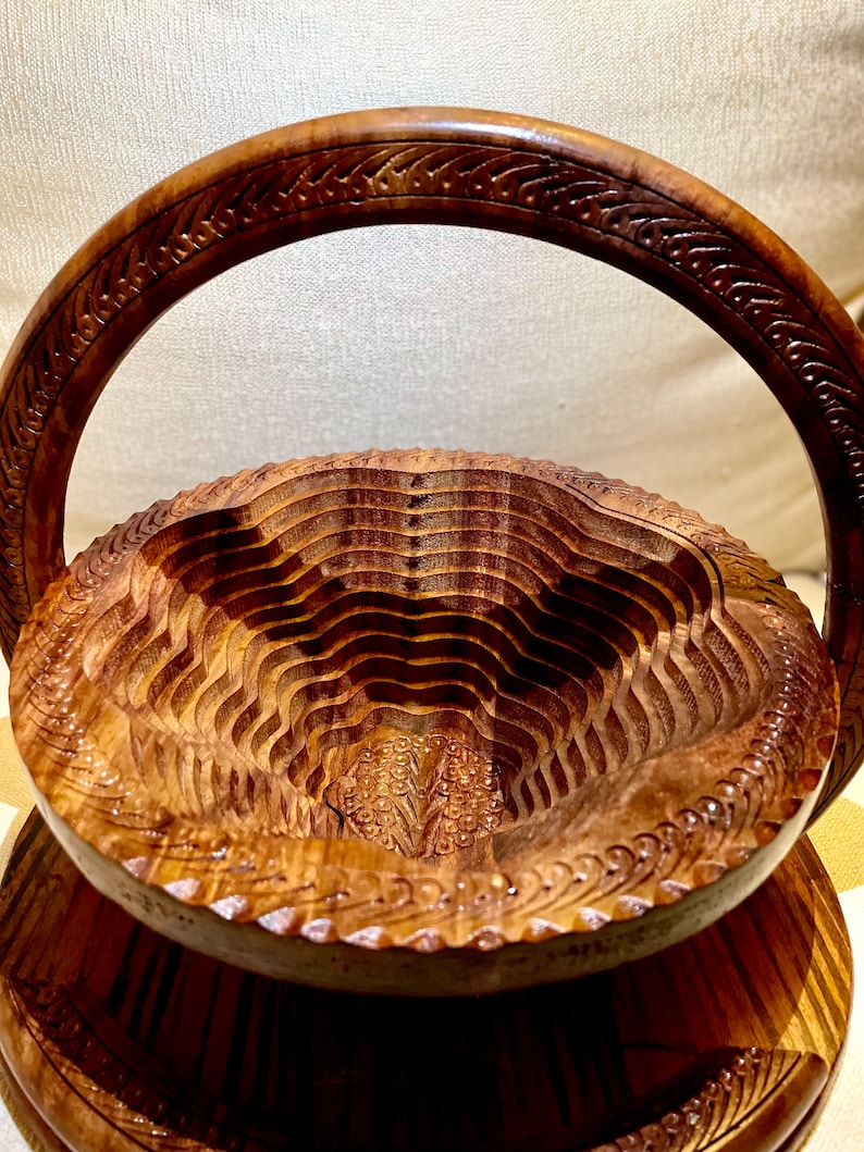 May include: A two-tiered wooden serving stand with a carved handle. The stand is made of dark brown wood and has a decorative design.