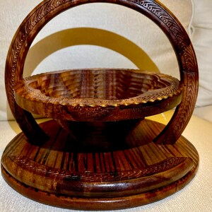 May include: A wooden fruit bowl with a carved handle. The bowl is made of dark wood and has a round shape. The handle is also made of wood and has a decorative design.