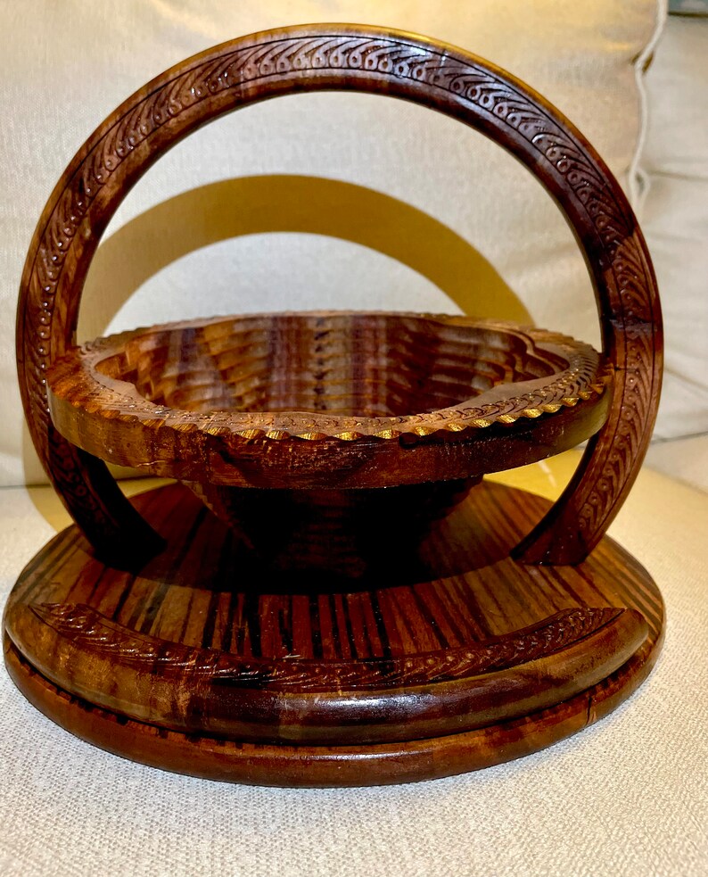 May include: A wooden fruit bowl with a carved handle. The bowl is made of dark wood and has a round shape. The handle is also made of wood and has a decorative design.