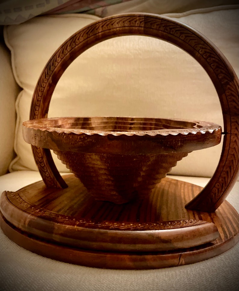 May include: A wooden bowl with a handle, the bowl is made of dark wood and has a carved design around the rim. The handle is also made of dark wood and has a carved design.