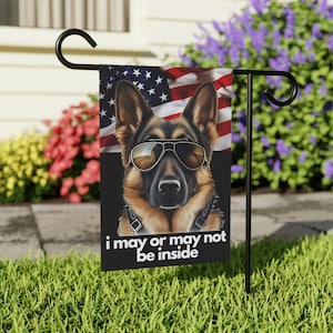 May include: A garden flag with a German Shepherd wearing sunglasses and a black collar. The flag has a red, white, and blue American flag design in the background. The text on the flag reads "i may or may not be inside".