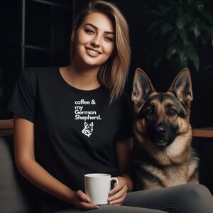 May include: A woman wearing a black t-shirt with the text "coffee & my German Shepherd."  She is holding a white coffee mug and sitting next to a German Shepherd dog.