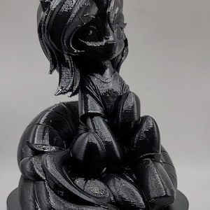 May include: A black 3D-printed figurine of a pony-like character with a horn, sitting on a round base. The figurine has a detailed mane, tail, and clothing, with a smooth, glossy finish. The character is in a seated position.