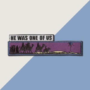 May include: An embroidered patch with a purple background and a scene of people walking with camels. The text "HE WAS ONE OF US" is on a white banner above the scene.