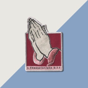 May include: Embroidered patch featuring a pair of hands clasped in prayer, on a red background with pink accents. The text "1 Thessalonians 5:17" is at the bottom of the patch.