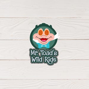 May include: A green circle with a cartoon frog face inside. The frog has large, red, wide-eyed pupils. The text "Mr. Toad's Wild Ride" is below the circle.