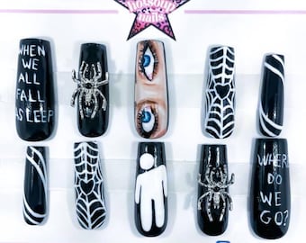 May include: A set of ten black and white press-on nails with various designs. The designs include a spider, spiderwebs, eyes, and text that reads "WHEN WE ALL FALL ASLEEP" and "WHERE DO WE GO?". A pink star logo is at the top.