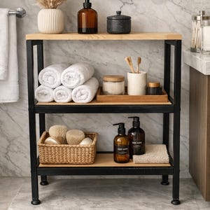 May include: A three-tiered bathroom shelf with a black metal frame and light wood shelves. The top shelf holds a brown glass soap dispenser, a black container, and a vase with dried flowers. The middle shelf has rolled white towels. The bottom shelf has a basket with bath sponges.