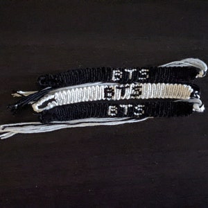 May include: Three black and white friendship bracelets with the word "BTS" woven into each one.