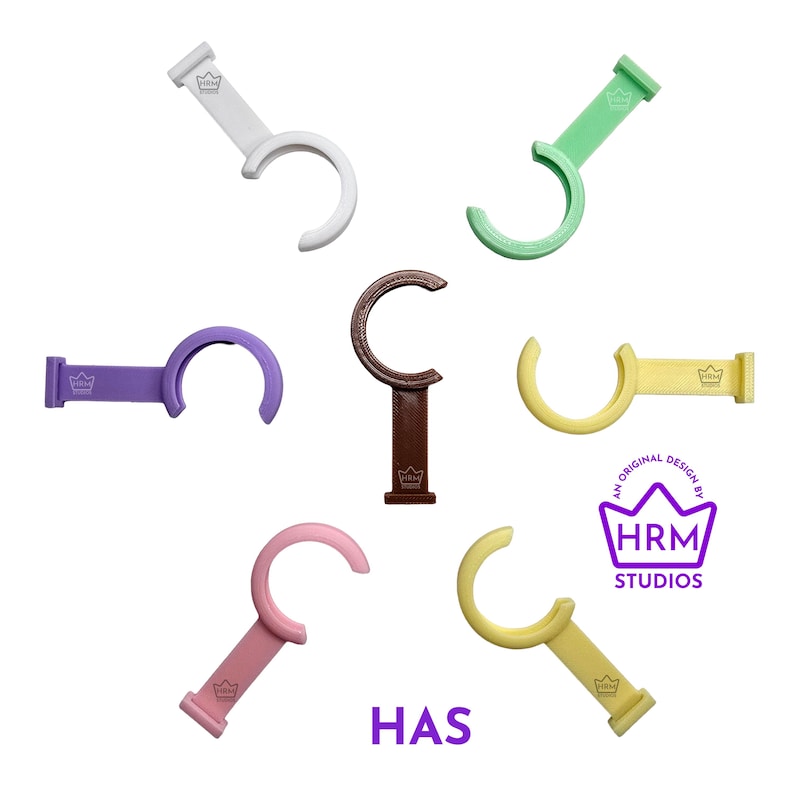Puede incluir: Una colecci&oacute;n de ganchos en forma de C de colores, en blanco, verde, morado, marr&oacute;n, amarillo y rosa. Cada gancho tiene una base rectangular con un logotipo de corona y el texto "HAS". La imagen tambi&eacute;n incluye el texto "AN ORIGINAL DESIGN BY HRM STUDIOS".