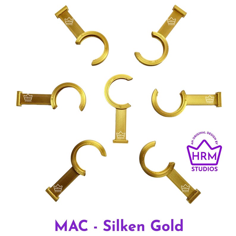 Puede incluir: Ganchos met&aacute;licos dorados con un dise&ntilde;o curvo, dispuestos en un patr&oacute;n circular sobre un fondo blanco. Los ganchos tienen una parte superior rectangular con un logotipo y el texto "MAC - Silken Gold" en la parte inferior.