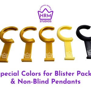 Puede incluir: Cinco colgantes para bl&iacute;ster en oro, amarillo y negro. Cada colgante tiene una parte superior curvada y una base rectangular con el logotipo "HRM Studios". El texto en la parte inferior dice "Special Colors for Blister Packs & Non-Blind Pendants."