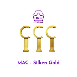 Puede incluir: Tres objetos met&aacute;licos dorados en forma de C con una base rectangular de malla. Los objetos est&aacute;n etiquetados como "MAC - Silken Gold" en texto p&uacute;rpura. La parte superior de la imagen presenta un logotipo p&uacute;rpura con el texto "HRM STUDIOS".