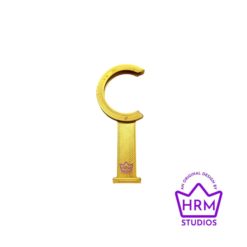 Puede incluir: Un gancho de cortina dorado con una barra vertical texturizada y una parte superior curvada. El gancho tiene una peque&ntilde;a base rectangular y un dise&ntilde;o decorativo. El logotipo "HRM STUDIOS" est&aacute; en la esquina inferior derecha.