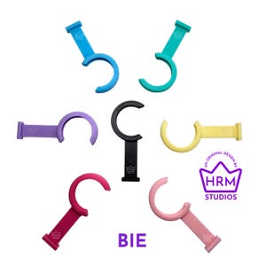 Puede incluir: Una colecci&oacute;n de abridores de botellas curvos y coloridos en varios tonos, incluyendo azul, verde, morado, negro, amarillo, rojo y rosa. Cada abridor presenta un mango y un dise&ntilde;o de gancho curvo. Tambi&eacute;n se ve el texto "BIE" y un logotipo.