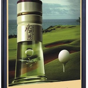 May include: A clear glass bottle with a white cap and a green liquid inside. The bottle is on a green grassy surface with a golf ball on a tee in the background. The bottle has Chinese characters on the label that read "水井坊".