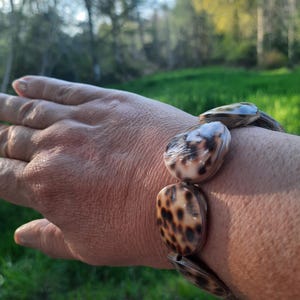 May include: A bracelet made of brown and white seashells. The bracelet is on a person's wrist.